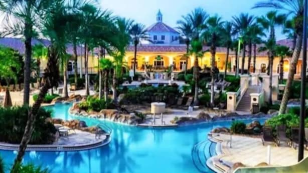 Un resort con una amplia piscina central, palmeras y un edificio con techo abovedado.