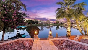 A serene lakeside setting with a pathway leading to a boat dock, palm trees, and a calm water body reflecting the sky. - Lakefront Resort Villa - Heated Infinity Pool & 8-Seat Spa - Kayaks - 4BR (Mesa)