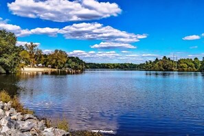 Un lac paisible avec un quai, entouré d’arbres et surplombé d’un ciel bleu clair.