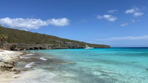A beach with clear turquoise water, rocky shoreline, and a boat in the distance. - Brand new luxurious villa with bay and mountain view (Curaçao)