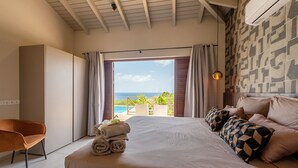 A bedroom with a large bed, a view of the sea, and a balcony with plants. - Brand new luxurious villa with bay and mountain view (Curaçao)