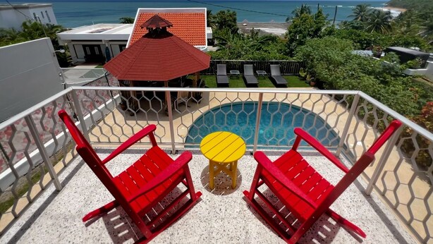 A balcony with a pool, red chairs, and a yellow table.