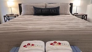 A hotel room with a bed, two bedside lamps, a framed artwork above the bed, and two towels with a floral design on a bench.