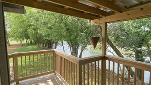 Une terrasse en bois dotée d’une rambarde, qui offre une vue sur une zone herbeuse et des arbres.
