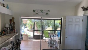 Een woonkamer met een bank, een eethoek met stoelen en een tafel, en een schuifpui die leidt naar een terras buiten met een zwembad en stoelen.
