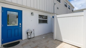Un bâtiment blanc avec une porte bleue, une petite fenêtre et une clôture blanche.