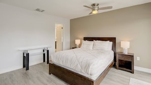 Une chambre à coucher comprenant un lit, des tables de chevet, un ventilateur de plafond et un bureau.