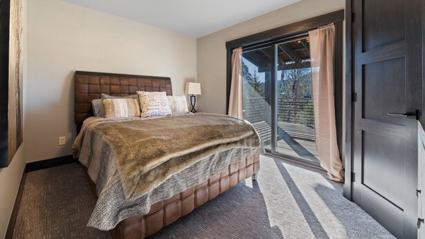 A bedroom with a large bed, a nightstand, a lamp, and a view of a balcony. - Restful Retreat with Panoramic Views, Hot Tub, and Centrally Located to Deadwood (Lead)