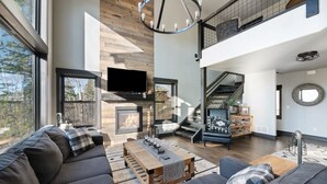 A modern living room with a fireplace, large windows, and a staircase leading to an upper level. - Restful Retreat with Panoramic Views, Hot Tub, and Centrally Located to Deadwood (Lead)