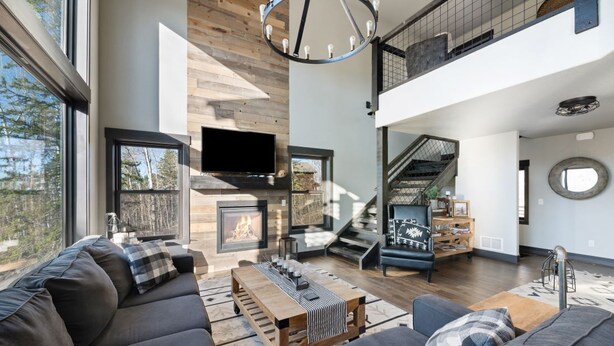 A modern living room with a fireplace, large windows, and a staircase leading to an upper level. - Restful Retreat with Panoramic Views, Hot Tub, and Centrally Located to Deadwood (Lead)
