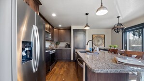 A modern kitchen with stainless steel appliances, wooden cabinets, a granite countertop island, and pendant lighting. - Restful Retreat with Panoramic Views, Hot Tub, and Centrally Located to Deadwood (Lead)