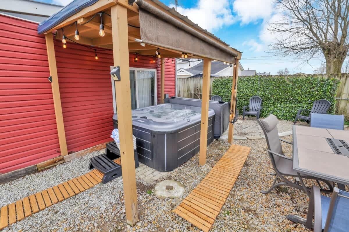 Un jardin avec un jacuzzi, un espace salon extérieur et une pergola illuminée de guirlandes lumineuses.