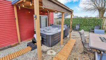 Un jardin avec un jacuzzi, un espace salon extérieur et une pergola illuminée de guirlandes lumineuses.