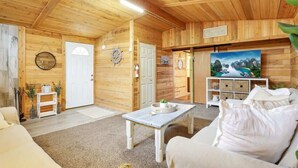 Interior acogedor de una cabaña de madera, con un sofá blanco, una mesita y un cuadro en la pared.
