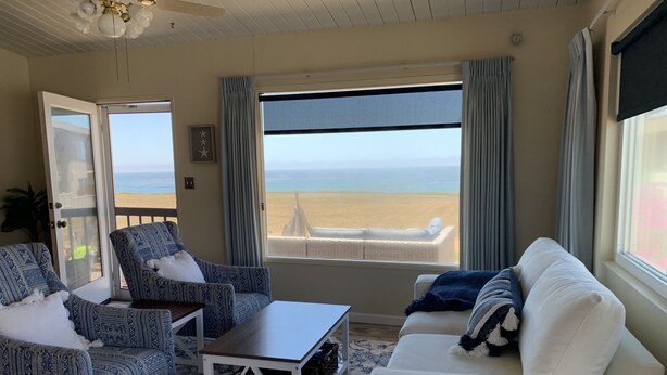 Habitación con vistas a la playa, que incluye un sofá blanco, sillones estampados y una mesa de centro de madera.