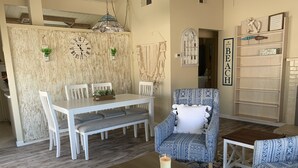 Un comedor con una mesa y sillas blancas, un sillón estampado y una vela sobre una mesa de madera.