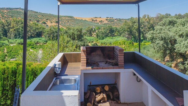 An outdoor kitchen area with a built-in grill, a sink, and a view of a hilly landscape. - Cubo's Casa Rio Grande / private pool / rural (Guaro)