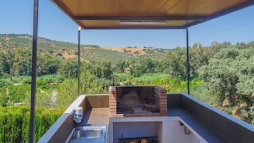 An outdoor kitchen area with a built-in grill, a sink, and a view of a hilly landscape.