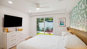 Ein Schlafzimmer mit einem Bett, einem Fernseher, einem Schminktisch und einer Schiebetür zum Balkon.
