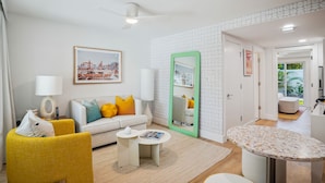 A modern living room with a sofa, yellow armchair, coffee table, and a mirror with a green frame. - Mello on the Beach - Shore Enuff (Holmes Beach)