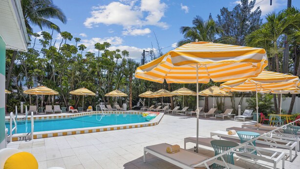 A poolside area with striped umbrellas, lounge chairs, and a swimming pool. - Mello on the Beach - Shore Enuff (Holmes Beach)