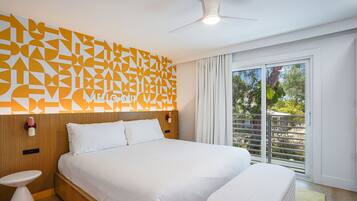 A modern hotel room with a large bed, a small bedside table, a ceiling fan, and a view of the outdoors through a large window.