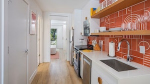 A modern kitchen with white cabinetry, a stainless steel sink, and a red tiled backsplash. - Mello on the Beach - Gone Coastal (Holmes Beach)