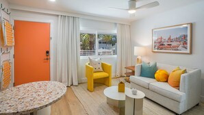 A modern living room with a round table, a sofa, a yellow armchair, and a large window with curtains. - Mello on the Beach - Gone Coastal (Holmes Beach)
