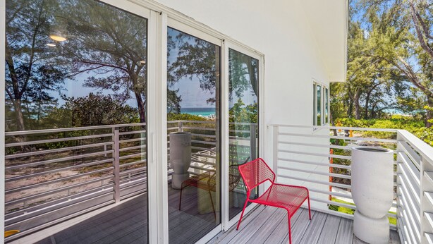A balcony with a red chair, a white railing, and a view of the beach and ocean. - Mello on the Beach - Slow M'Ocean (Holmes Beach)