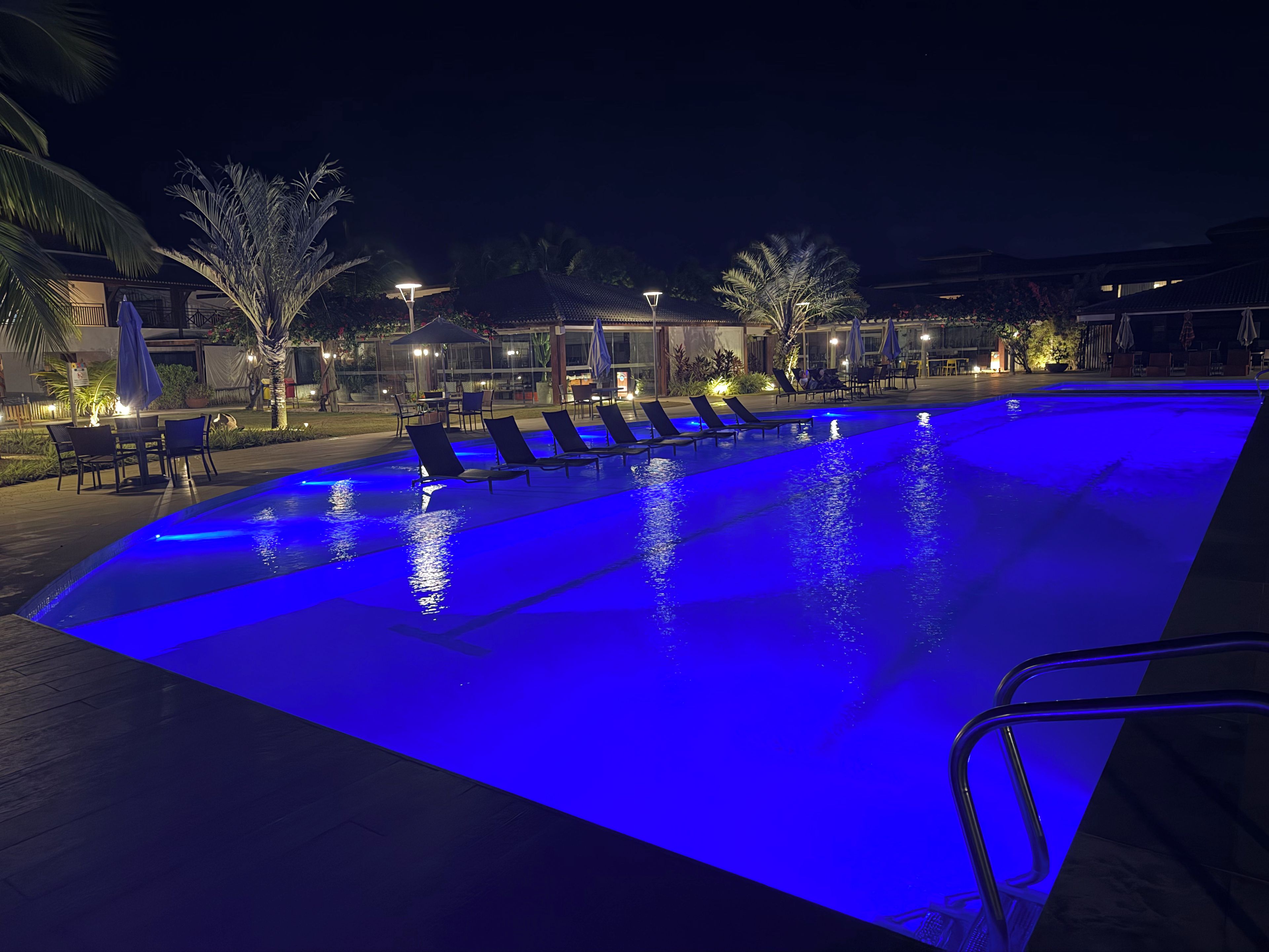 A swimming pool with blue lighting, lounge chairs, and outdoor seating.