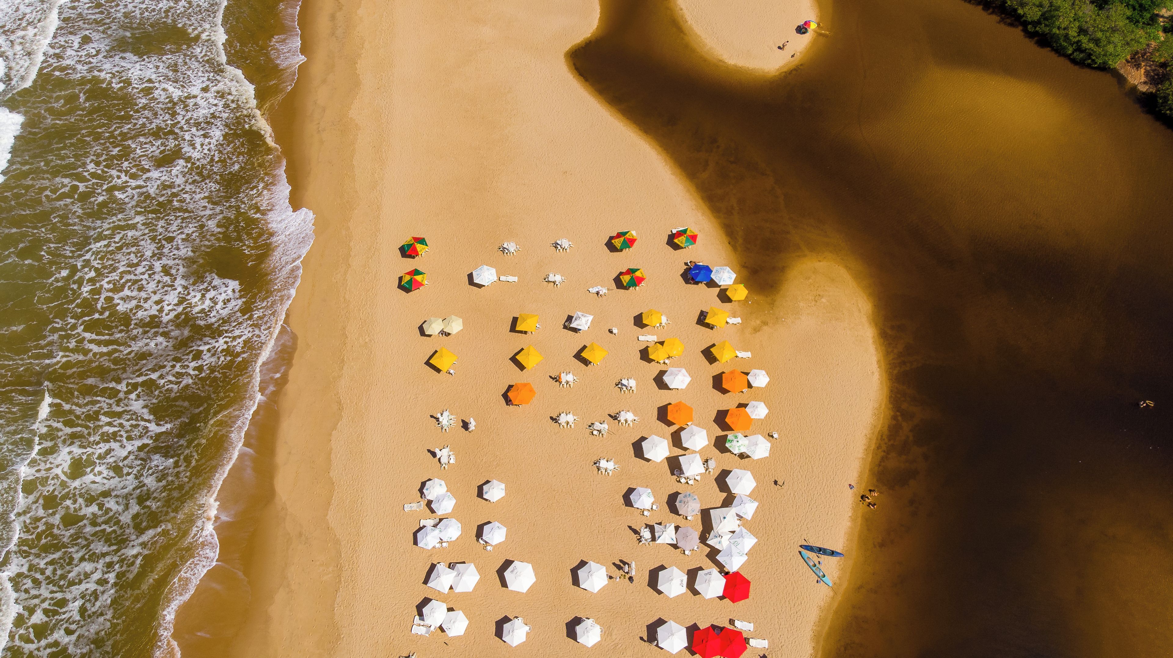 An aerial view of a beach with numerous umbrellas and beach chairs arranged in rows.