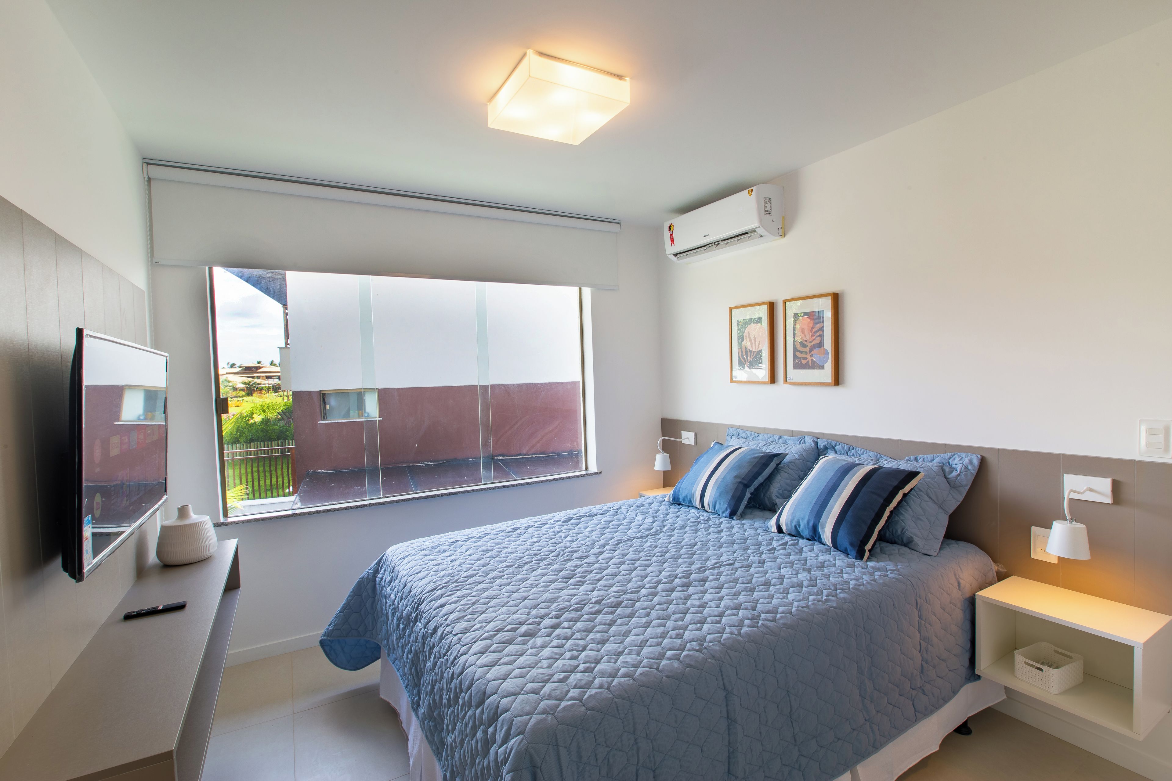 A bedroom with a large bed, bedside tables, a window, and an air conditioning unit.