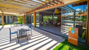 An outdoor patio area with tables and chairs, a wooden pergola, and a sign indicating a restaurant. - Areia Azul Aparts Brazil - Imbassai Ykutiba (Mata de São João)