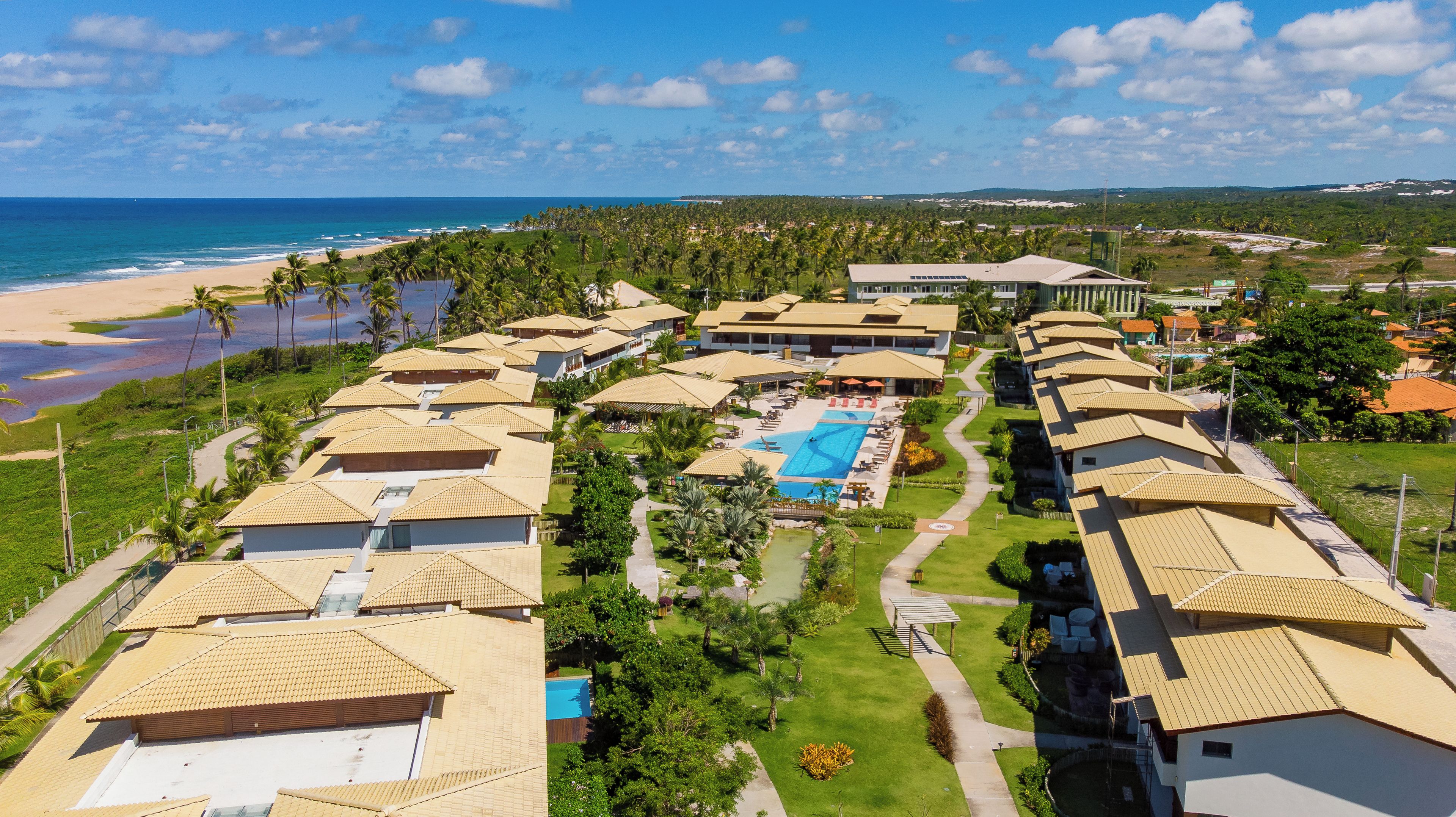 A resort with multiple bungalow-style buildings, a central swimming pool, and a beach view.