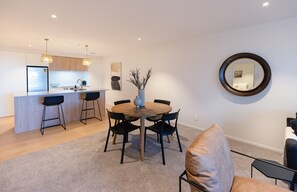 Une cuisine moderne avec un îlot central, des chaises noires disposées autour d’une table en bois et un miroir rond accroché au mur.