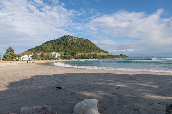 Une plage avec une montagne en arrière-plan, un ciel dégagé et quelques bâtiments près du rivage.