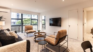 Ein modernes Wohnzimmer mit einer Couch, Sesseln, einem Couchtisch und einem flachbildfernseher, der an der Wand montiert ist.