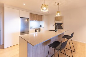 Une cuisine moderne dotée d’un îlot central, d’appareils électroménagers en acier inoxydable et de tabourets de bar noirs.