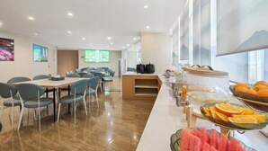 Espaço de refeições de hotel com serviço de buffet, incluindo frutas e bebidas.