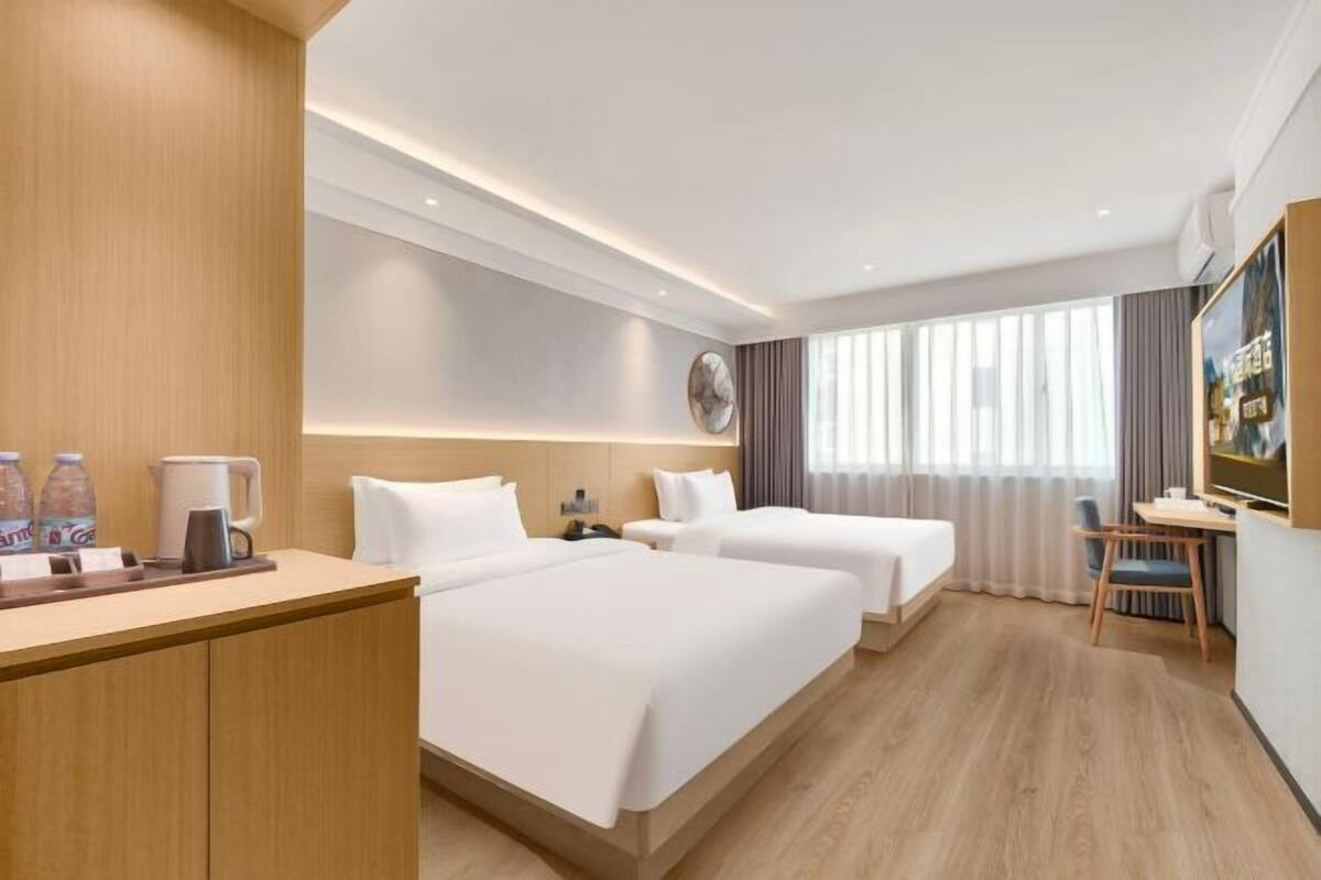 Une chambre d’hôtel avec deux lits, un bureau, une chaise, une télévision et une grande fenêtre avec des rideaux.