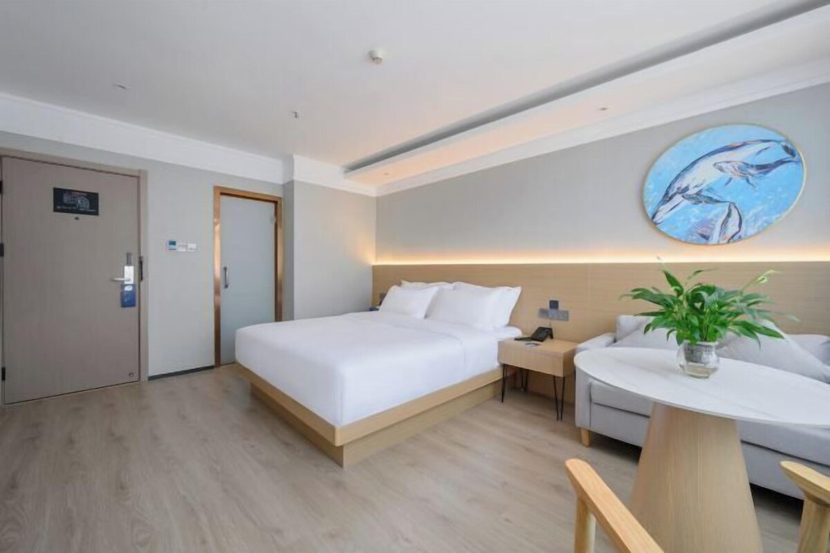 A modern hotel room with a large bed, a round table with a plant, a sofa, and a painting of dolphins on the wall.