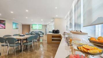 A modern dining area with a long counter, seating, and a buffet with fruits.