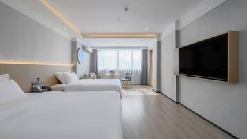 Une chambre d’hôtel avec deux lits, un téléviseur à écran plat fixé au mur, une petite table avec une chaise et une fenêtre avec des rideaux.