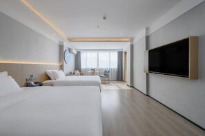 A hotel room with two beds, a flat-screen TV mounted on the wall, a small table with a chair, and a window with curtains.