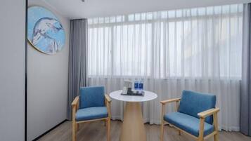 A room with two blue chairs, a round wooden table, and a painting on the wall.
