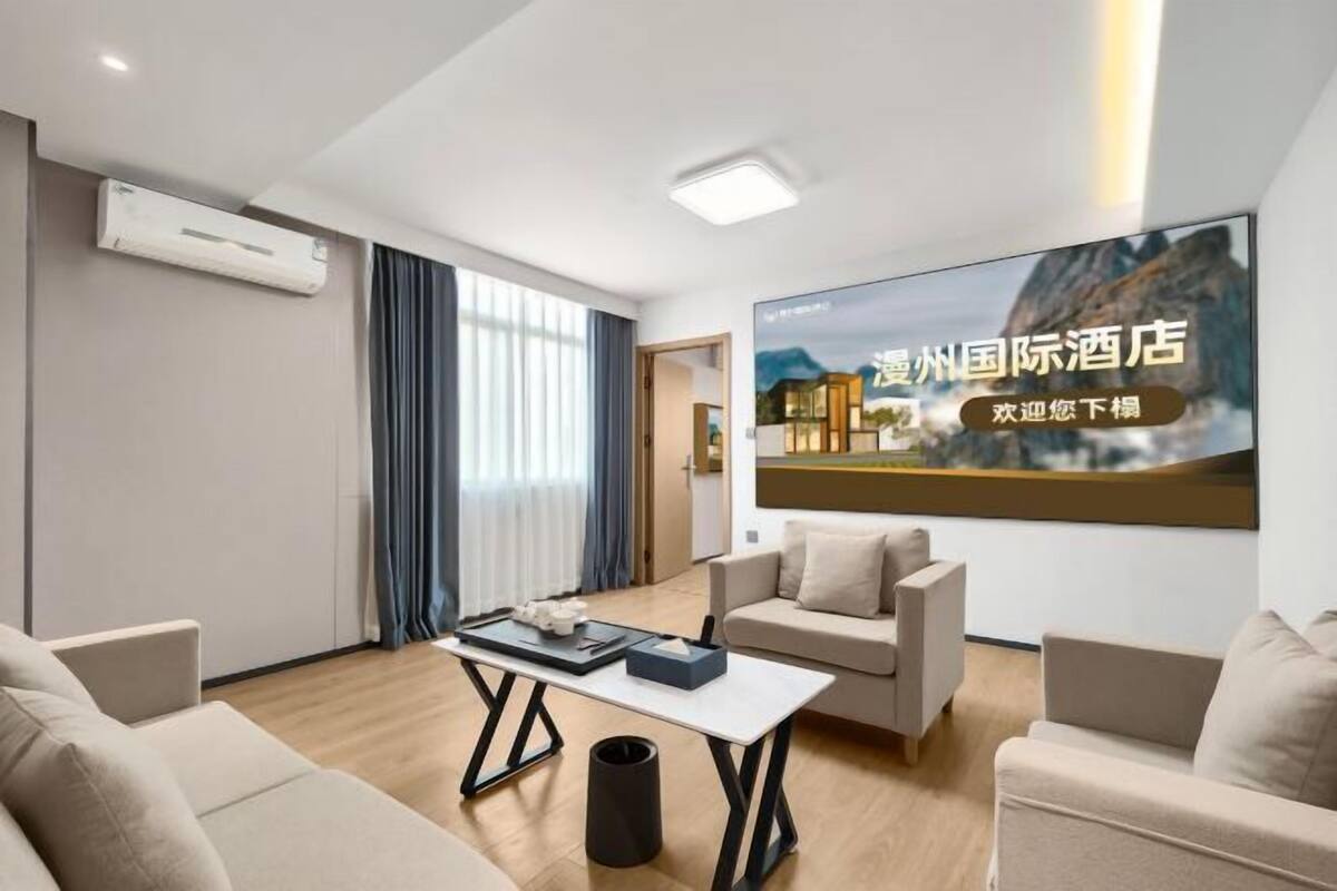 Une chambre d’hôtel moderne dotée d’un grand écran de télévision diffusant un paysage magnifique, d’un canapé, d’une table basse et d’un appareil de climatisation.