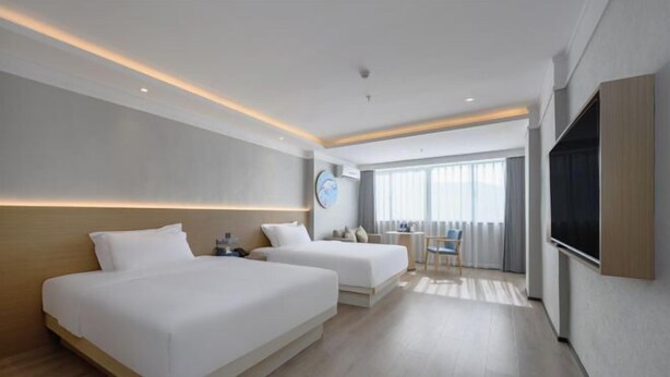 Quarto de hotel moderno com duas camas, uma escrivaninha, uma cadeira, televisão e uma janela grande com cortinas.