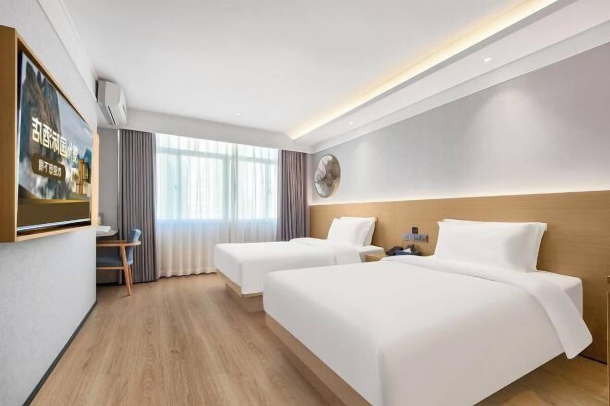 Une chambre d’hôtel avec deux lits, un bureau, une chaise et une grande fenêtre avec des rideaux.