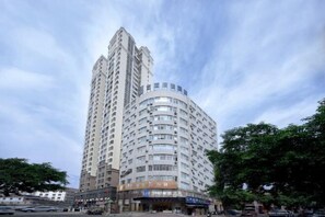 A tall, multi-story hotel with a curved facade, featuring a ground-level commercial area with various shops.