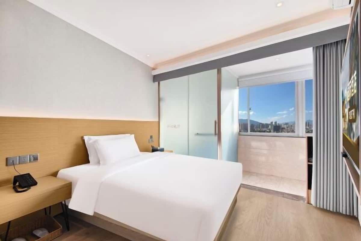 Une chambre d’hôtel moderne, équipée d’un lit, d’une table de chevet et offrant une vue sur la ville.